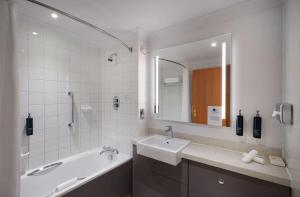 a bathroom with a sink and a bath tub and a mirror at DoubleTree by Hilton Swindon Hotel in Swindon