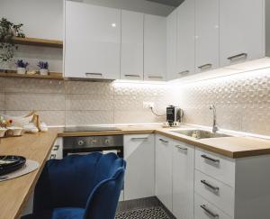 a kitchen with white cabinets and a sink and a blue chair at Delta - Central Elegant Apartment in Katerini