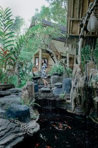 a person standing in front of a house with a pond at Abing Dalem - Villa Durian in Tabanan