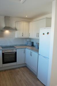 a kitchen with white cabinets and a white refrigerator at Sunny Side Up Beach House in Tywyn in Tywyn