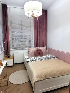 a bedroom with a pink bed and a chandelier at APARTAMENT JARACZA 28/11 in Słupsk