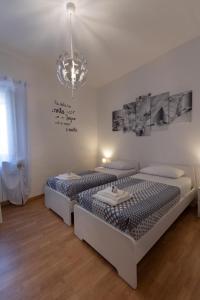 Habitación blanca con 2 camas y lámpara de araña. en Casa vacanze Il Pugnalone, en Acquapendente