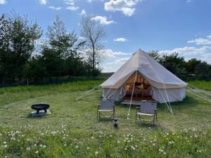 a tent with two chairs and a table in a field at Mellem-rummet Guesthouse & Glamping in Tanderup