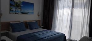 a bedroom with a bed with blue pillows and a window at Anxhelos Hotel in Himare