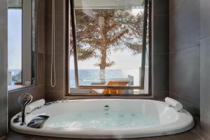 a bath tub in a bathroom with a large window at White Rocks Hotel Kefalonia in Lassi