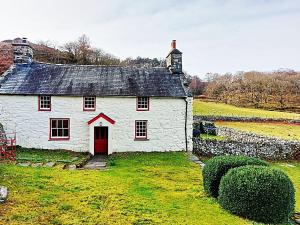a white house with a red door in a field at Gallestra a Rustic, Rural Retreat Farm House Nr Dolgellau Snowdonia in Dolgellau