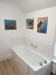 a white bathroom with three paintings on the wall at Chinwin Cottage in Weymouth