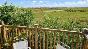 a wooden deck with two chairs and a field at Stable Barn Apartment in Saint Breward