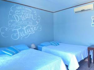two beds in a room with a blue wall at Hotel Perico Azul & Surf Camp in Jacó
