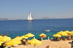 a beach with yellow umbrellas and a sail boat in the water at Aquarius Hotel in Kaş