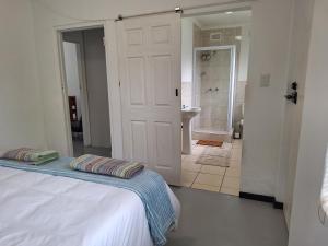a white bedroom with a bed and a bathroom at Siesta Cottage in Howick