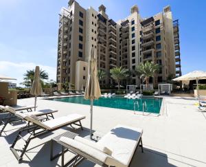 Cozy 1BR Retreat, Asayel 3 Madinat Jumeirah Living - 81AB0 في دبي: مسبح مع كراسي ومظلات أمام المبنى