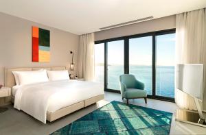 Le Méridien Bodrum Beach Resort في بوغازيتْشي: غرفة نوم بسرير ابيض وكرسي ازرق