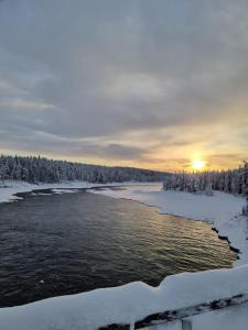 a river in the snow with the sunset in the background at Överkalix Kalixalven Lodge Jockfall in Jock