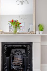 un miroir au-dessus d'une cheminée avec un vase de fleurs dans l'établissement Vogue 1 bedroom Pimlico flat near Victoria Station, à Londres