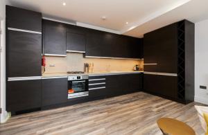 een keuken met zwarte kasten en een houten vloer bij The Harlesden Escape - Spacious 3BDR Flat with Balcony in Londen