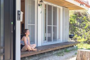 a woman sitting on the porch of a house at totono house 満天の星空 テントサウナ BBQ 元有形文化財を1棟貸切 うるま市 浜比嘉島 in Uruma