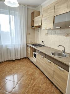 eine Küche mit Holzschränken, einem Waschbecken und einem Fenster in der Unterkunft Decebal 2 in Chişinău
