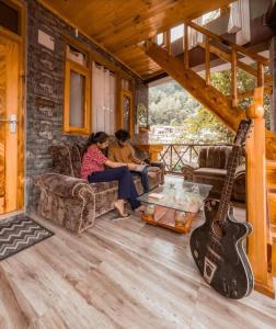 dos personas sentadas en un porche con una guitarra en Hodophile Home Manali, en Manali
