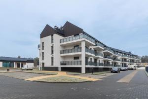 ein großes weißes Gebäude mit Autos auf einem Parkplatz in der Unterkunft Flatbook Apartamenty - Jantar Resort in Jantar