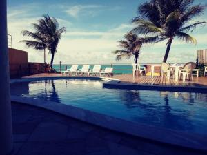 a swimming pool with chairs and palm trees and the ocean at Atlântico Flat in Natal +13 photos