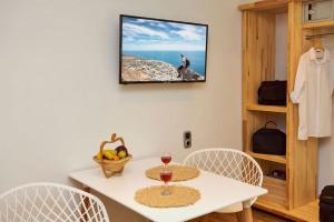 einen weißen Tisch mit 3 Stühlen und einen TV an der Wand in der Unterkunft Apartments Gonies - Dimitra in Avdou