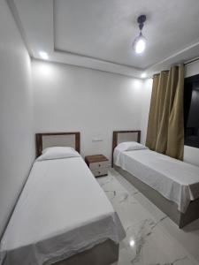 2 camas en una habitación con paredes blancas y ventana en Appartement moderne près de la corniche, en Nador
