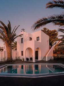 a white house with palm trees and a swimming pool at Nobu Hotel Santorini in Imerovigli