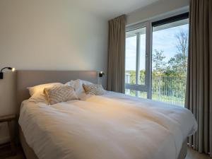 Un dormitorio con una gran cama blanca con ventana. en Apartment Veerse Meer with Private Marina, en Arnemuiden