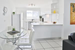 a white kitchen with a glass table and white chairs at 112 Olive Apartments in Mildura