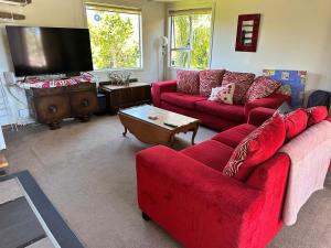 un soggiorno con divani rossi e TV di Cooks Beach Holiday Home a Cooks Beach