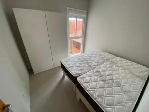a small bed in a room with a window at Ótimo apto 50m da areia churrasq 2Q 2 banheiros 301 in Torres
