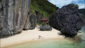 a group of people walking on a beach with rocks at Just Inn2 beachfront in El Nido