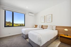 2 camas en una habitación blanca con ventana en Puggle Lodge en Jindabyne