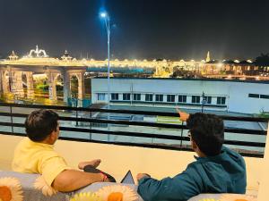 dos hombres sentados en una cornisa mirando un barco en Tiwari G Shridhara Hotel, en Ujjain