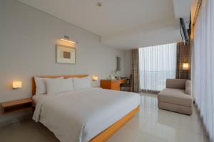 a bedroom with a large white bed and a chair at The Capital Hotel Surabaya in Surabaya