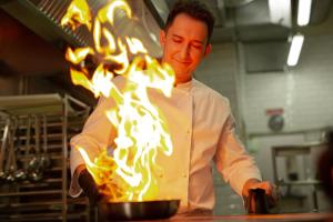 a man in a kitchen with a pot filled with fire at Hotel Miramare - SPA & Suites - Breakfast & Brunch Until 13-00 in Cervia