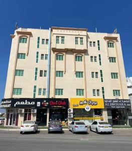 un gran edificio con coches estacionados frente a él en ALJAWHARA INN HOTEL, en Seeb