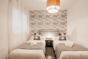 Cette chambre comprend 3 lits et un mur avec du papier peint. dans l'établissement tuGuest Maria Luisa Apartment, à Grenade