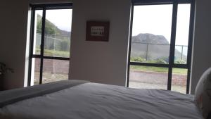 Schlafzimmer mit zwei großen Fenstern und einem weißen Bett in der Unterkunft Blombos Self-Catering House in Franskraalstrand