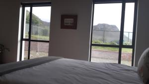 a bedroom with two large windows and a white bed at Blombos Self-Catering House in Franskraalstrand