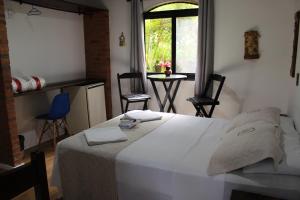 a bedroom with a white bed with chairs and a window at Pousada Manacas in Ubatuba