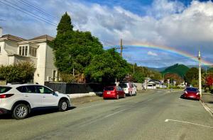 a rainbow in the sky over a street with parked cars at Honeysuckle House in Nelson