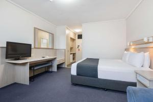 a hotel room with a bed and a desk with a television at Comfort Inn Glenelg in Adelaide