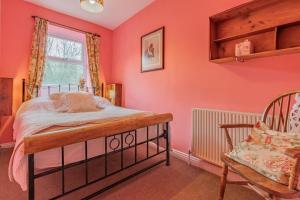 a bedroom with pink walls and a bed and a chair at Millpond Cottage in Holmfirth