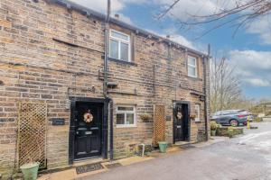 a brick building with two black doors on it at Millrace Cottage in Holmfirth