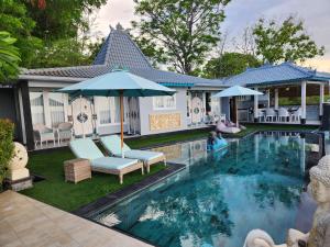 una piscina con sillas y sombrillas junto a una casa en The Kayu Manis Villa, en Lovina