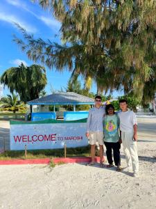 un gruppo di persone che si trovano di fronte a un cartello di benvenuto a Miami di Gaskara Guesthouse a Shaviyani Atoll