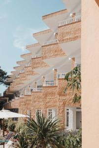 a brick building with white balconies and palm trees at Hotel Xaloc Playa in Punta Prima