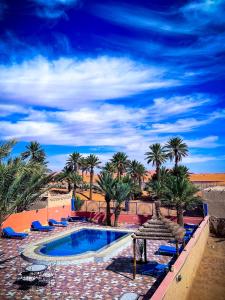 a swimming pool with palm trees and blue lounge chairs at Riad Les Roches Merzouga in Merzouga